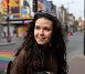 Woman with long dark hair standing on a street with buildings in the background